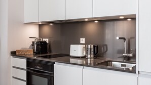 A modern kitchen with white cabinets, a black dishwasher, a coffee maker, and a kettle.