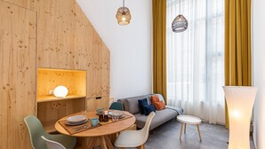 A modern dining area with a wooden wall, a round table, and chairs. There is a sofa and a window with curtains. - Waou Modern Loft III Centre (Madrid)