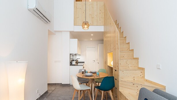A compact living space with a dining area, kitchen, and a wooden staircase. - Waou Modern Loft III Centre (Madrid)