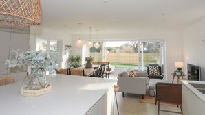 Eine moderne Küche mit Kochinsel, Essbereich mit einer Couch und Blick auf den Garten durch große Fenster.