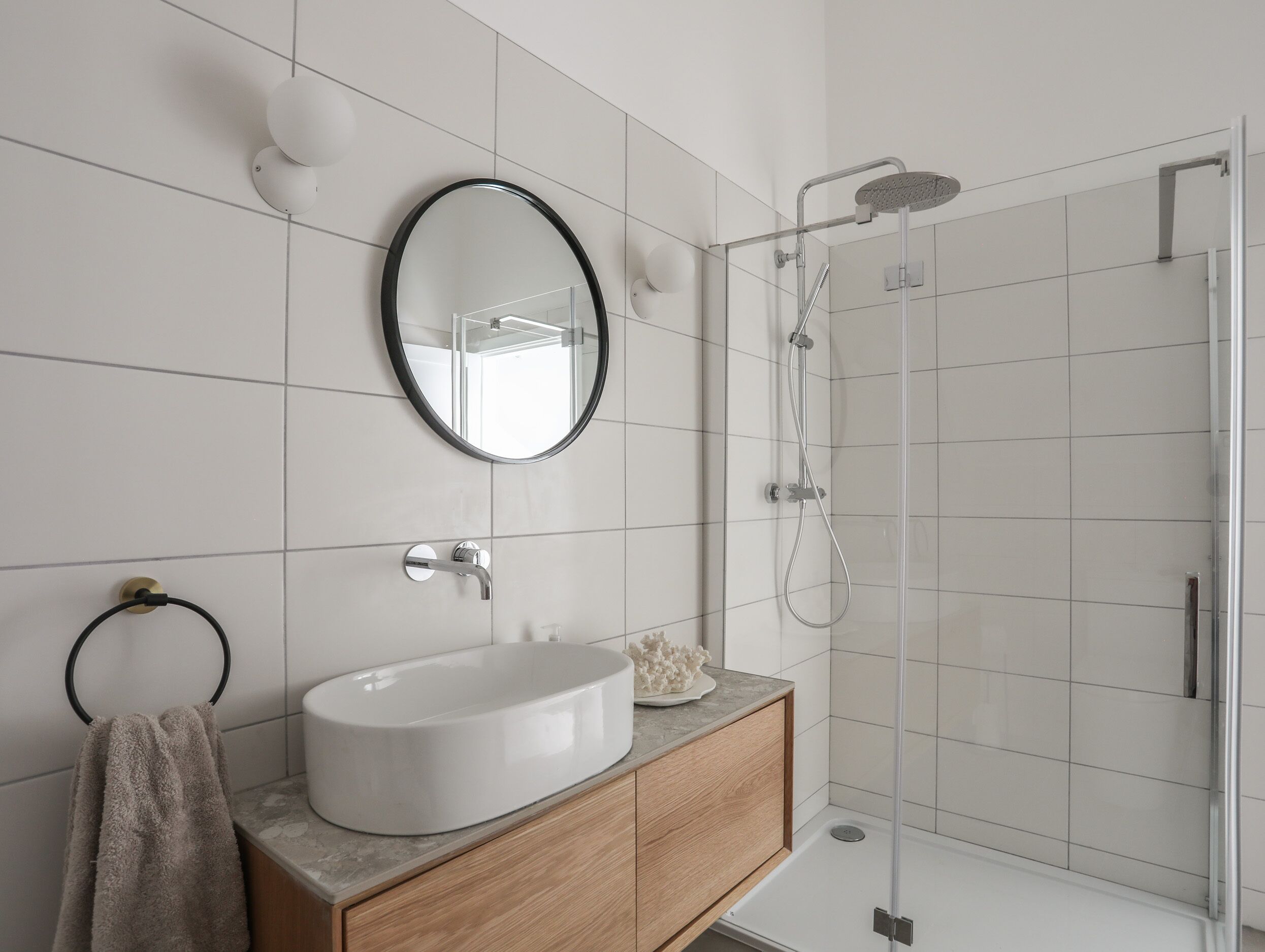 Une salle de bain moderne avec un miroir rond, un lavabo blanc et une douche à parois de verre.