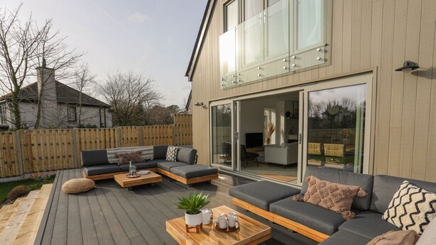 Ein moderner Außenbereich mit Holzboden, grauen Sofas und einem Couchtisch aus Holz, mit Pflanze und Dekorationselementen.