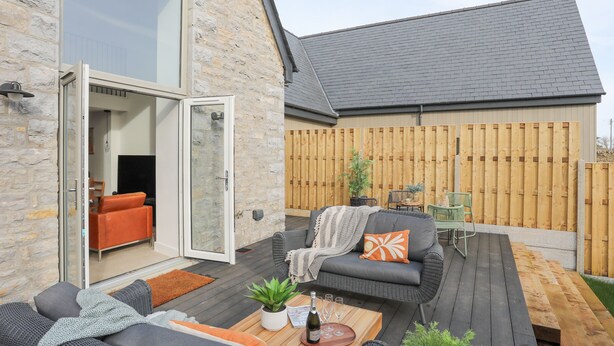 A patio with outdoor furniture, a wooden deck, and a stone wall. - Ysgol Fach (Tyn-y-Gongl)