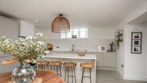 A modern kitchen with a round wooden table, bar stools, and a hanging light fixture. - Ysgol Fach (Tyn-y-Gongl)