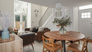 A spacious living area with a wooden dining table, leather sofa, and a staircase leading to an upper floor. - Ysgol Fach (Tyn-y-Gongl)