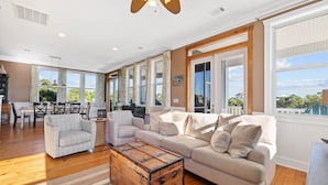 A spacious living room with a large sofa, a wooden chest, and a dining area with a table and chairs.