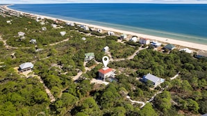 An aerial view of a coastal area with a beach, houses, and dense greenery.
