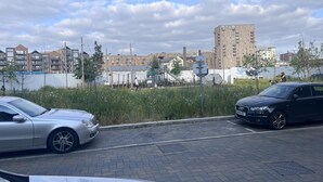 A parking area with cars, a building in the background, and a grassy area with trees.