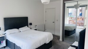 A modern bedroom with a large bed, a bedside table, a lamp, a wardrobe, and a sliding glass door leading to a balcony.