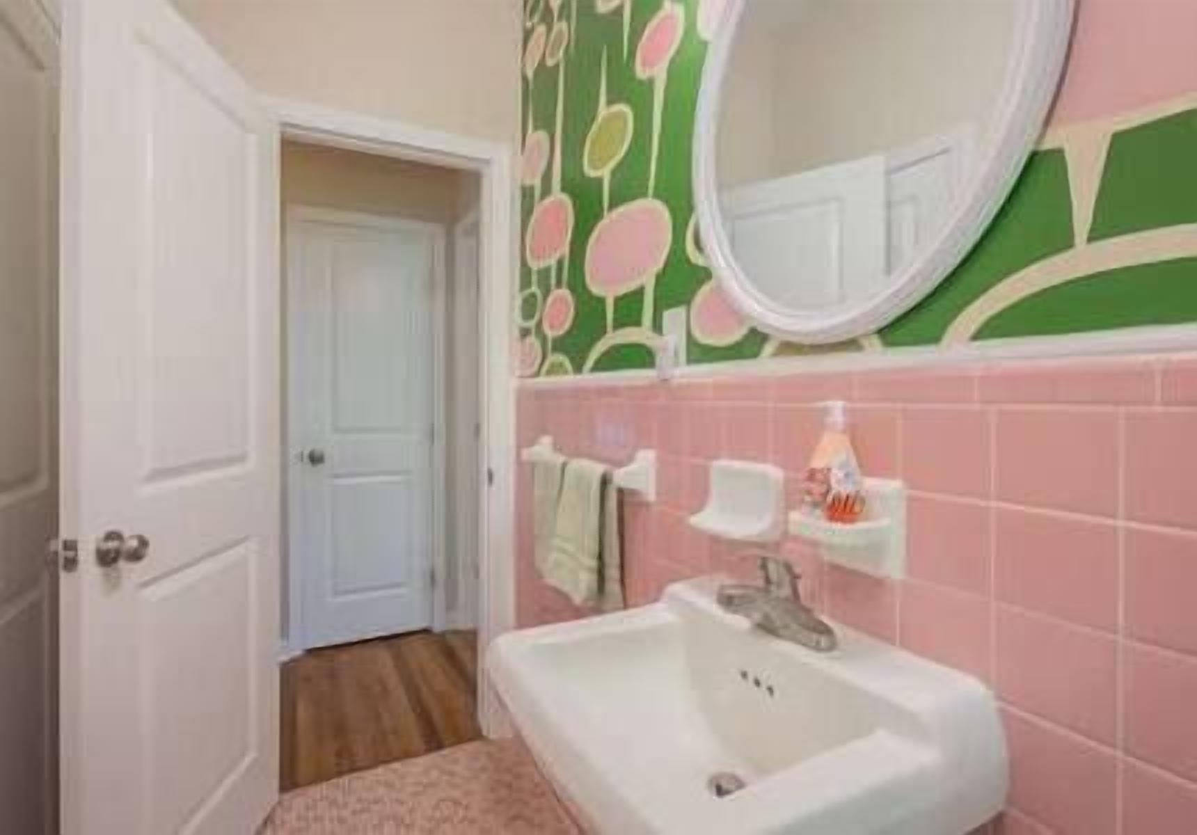 A bathroom with a white sink, pink tiles, a green and white patterned wall, and a white door.