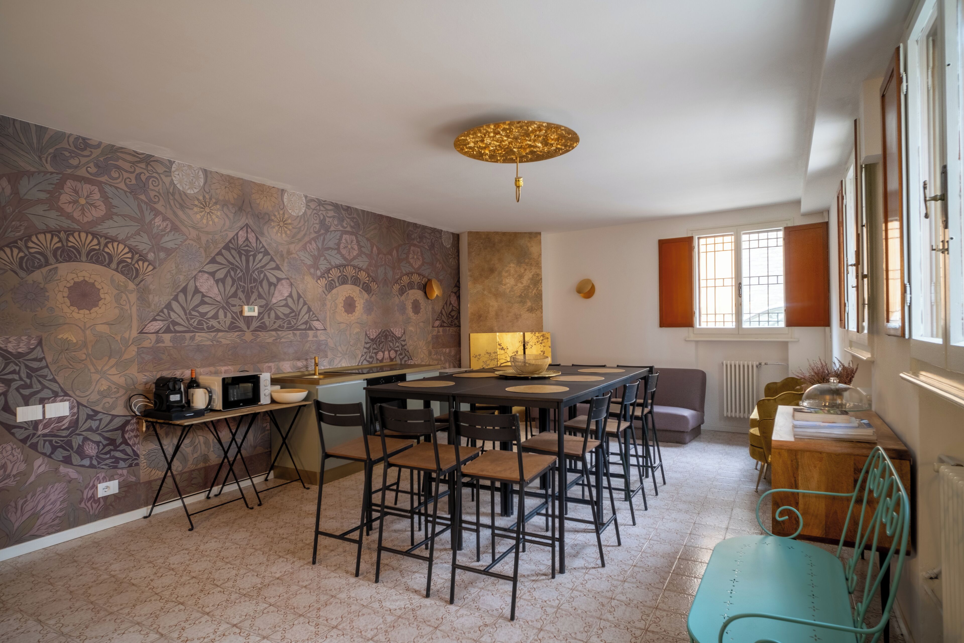 Un coin repas avec un mur décoré de motifs, une table avec des chaises, un luminaire suspendu et une fenêtre avec des stores.