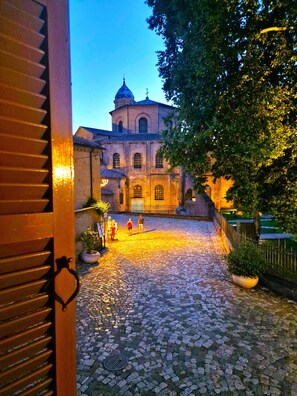 A cobblestone courtyard with a building featuring arched windows and a dome, surrounded by trees and a fence. - House 30 meters from the UNESCO monuments of San Vitale and the Galla Placidia (Ravenna)