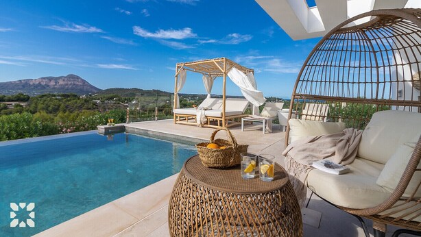 Zona de piscina con vista a la montaña, una silla de mimbre, una mesa de mimbre con una cesta y vasos, y una estructura tipo dosel.