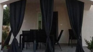 Un espacio al aire libre cubierto con mesa y sillas, adornado con cortinas negras, y un balcón superior.