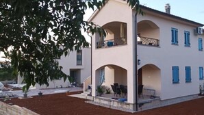Un edificio de dos pisos con balcón, un porche cubierto y un camino de entrada.