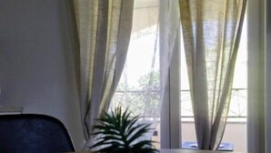 Una habitación con una mesa de comedor, una planta en maceta y una ventana con cortinas translúcidas.