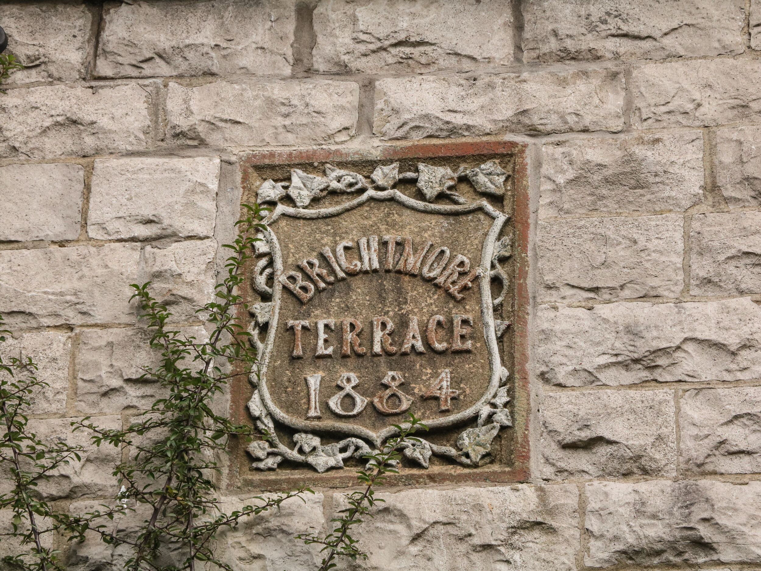A stone plaque with the inscription "BRIGHTMORE TERRACE 1884" on a stone wall.