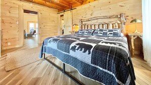 Un dormitorio de cabaña de madera con una cama grande, una araña y un cabecero rústico.