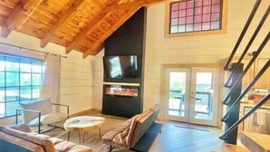 Amplia sala de estar con techo alto, chimenea, televisor y escalera que conduce a un nivel superior.