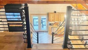Una habitación con techos altos, una escalera de madera, vista a una cocina y una puerta que conduce a otra estancia.