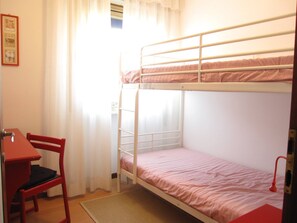 A bunk bed room with a desk and chair, a window with curtains, and a small picture frame on the wall.