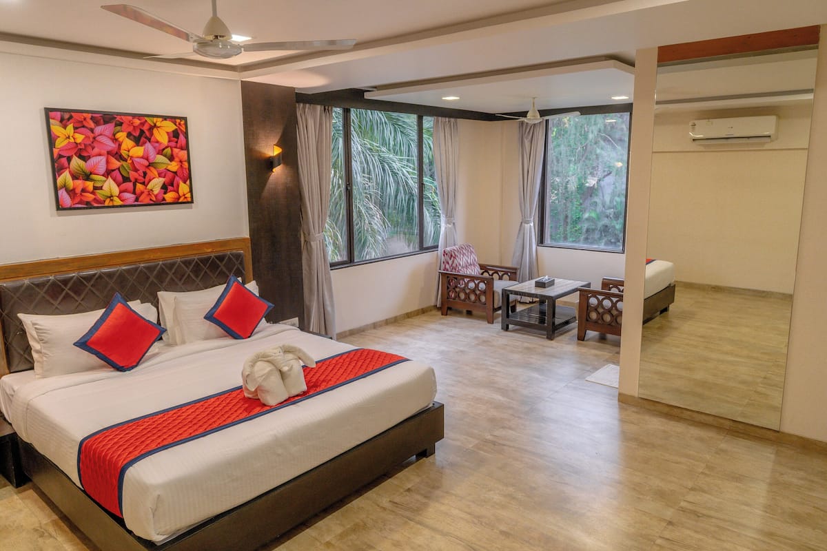 A hotel room with a bed, a desk, a chair, a window with curtains, an air conditioning unit, and a ceiling fan.