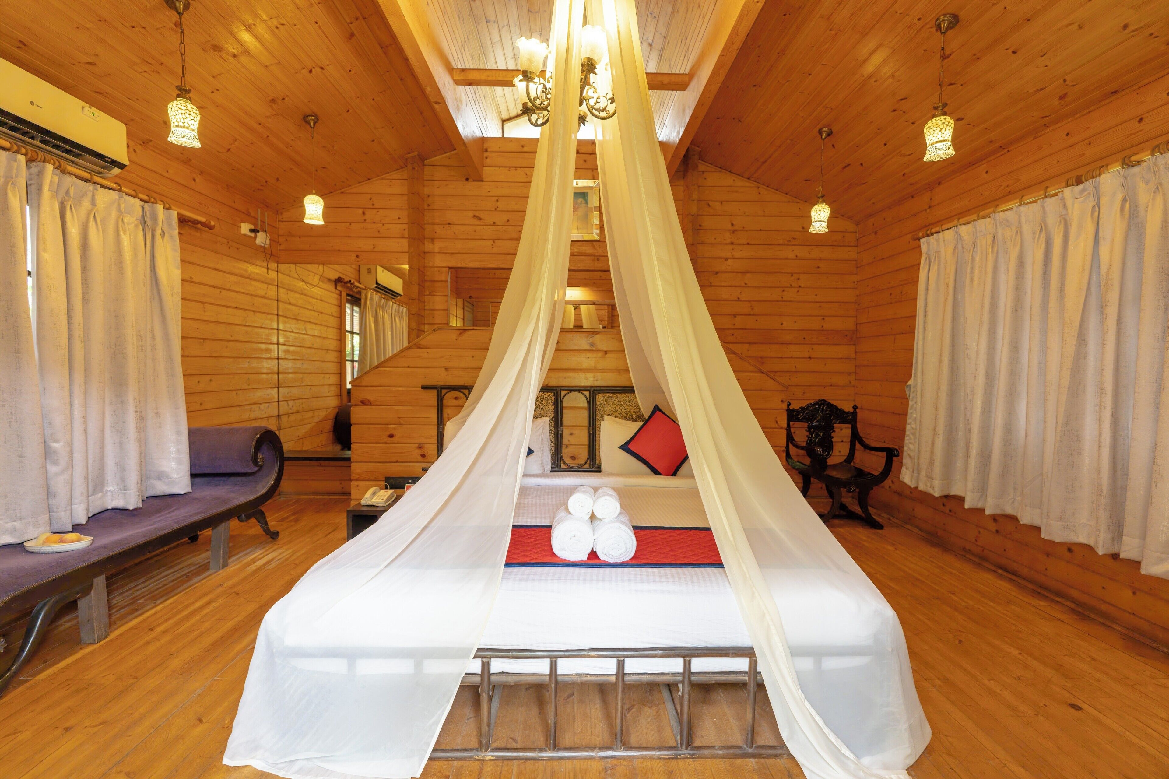 A wooden cabin room with a bed, a bench, and a staircase.