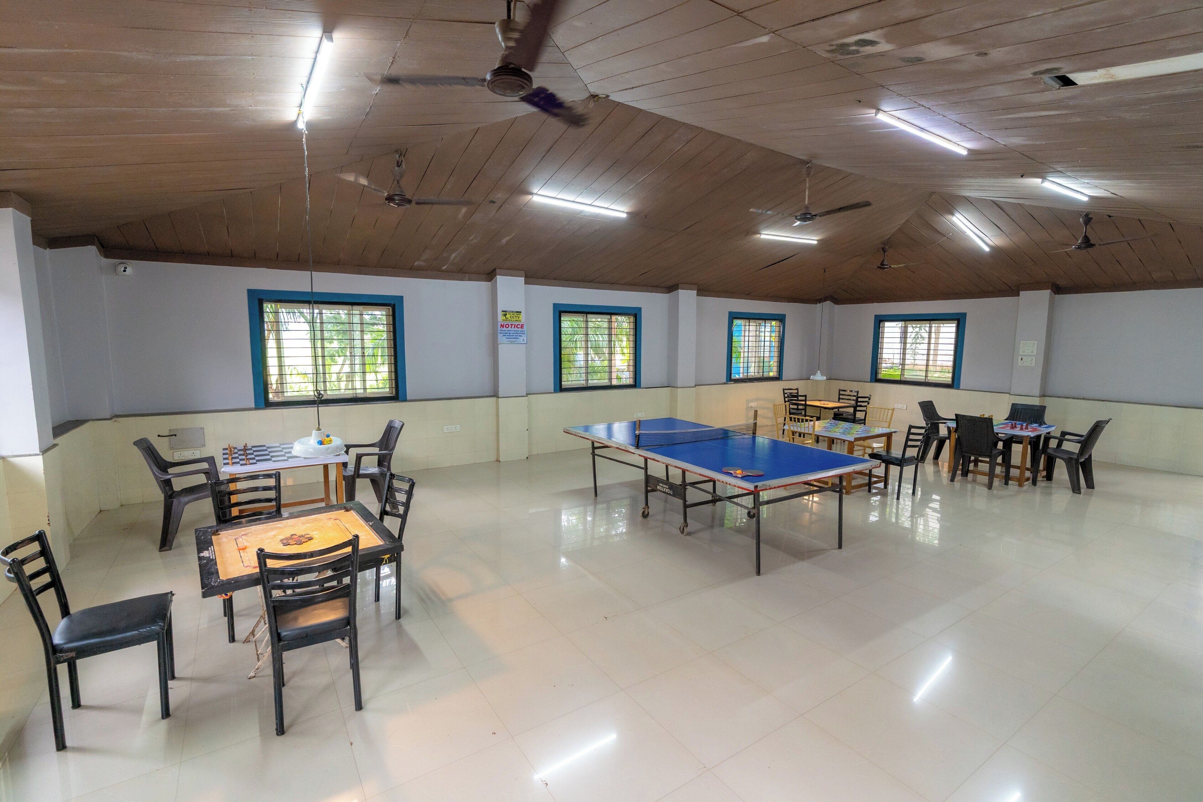 Un espacio interior amplio con mesa de ping pong, varias sillas y ventiladores de techo.