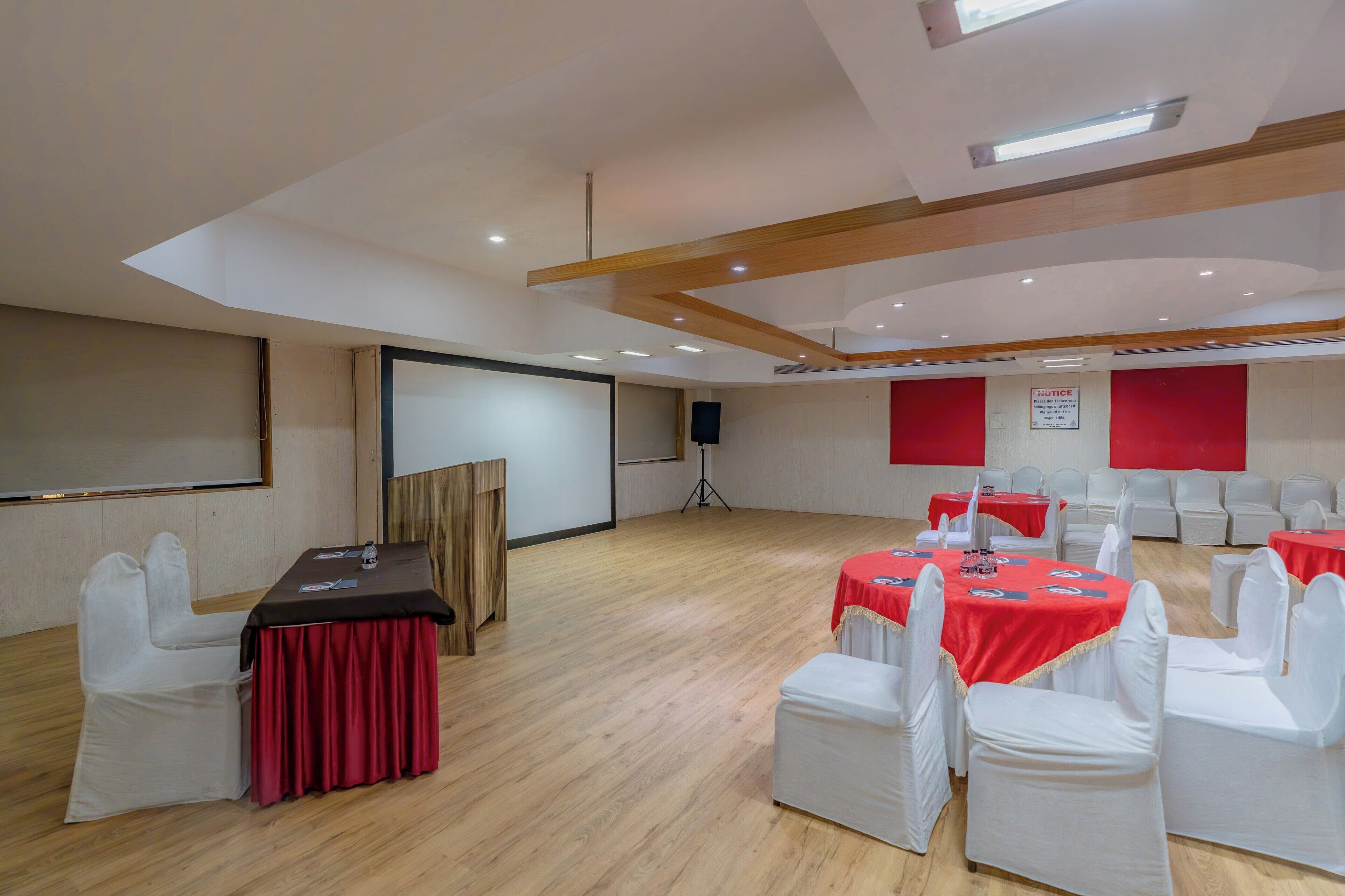 Un salón de conferencias con un escenario, sillas blancas y mesas cubiertas con manteles rojos.