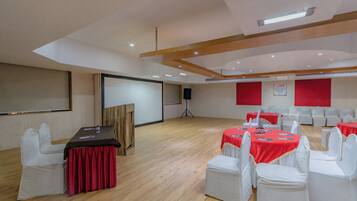 Un salón de conferencias con un escenario, sillas blancas y mesas cubiertas con manteles rojos.
