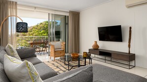 A modern living room with a sofa, a glass coffee table, a TV, and a balcony with a chair and table. - The Odyssey 302 (Cape Town)