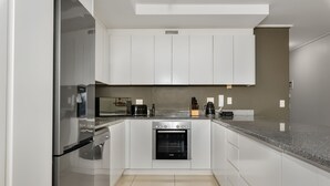 A modern kitchen with white cabinets, stainless steel appliances, and a granite countertop. - The Odyssey 302 (Cape Town)