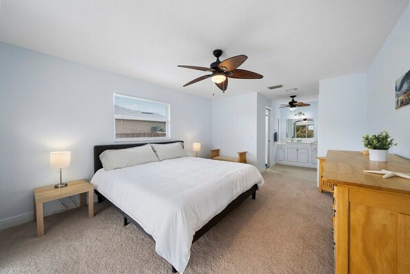 A bedroom with a bed, bedside tables, a ceiling fan, and a small desk with a plant. - New Reno w/ Pool, Fast Wi-Fi, Central Location (Cape Coral)