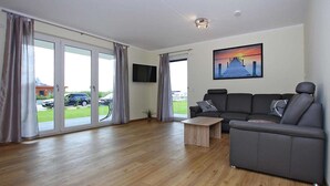 Ein modernes Wohnzimmer mit einem grauen Sofa, einem Holztisch und einem flachbildfernseher an der Wand.