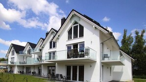 Ein modernes, zweistöckiges Haus mit Balkon im oberen Geschoss, großen Fenstern und einem gepflegten Rasen.
