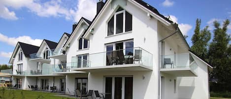 A modern two-story house with a balcony on the upper floor, large windows, and a well-maintained lawn.