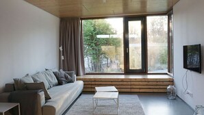A modern living room with a sofa, a coffee table, and a large window with a view of trees. - Design Ferienwohnung Nienrausch Apartment 1 (Timmendorfer Strand)