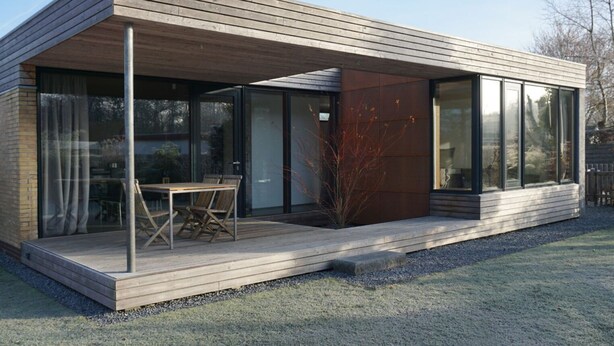 A modern house with a wooden deck, large windows, and a glass door. - Design Ferienwohnung Nienrausch Apartment 1 (Timmendorfer Strand)