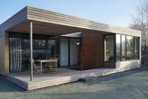 Ein modernes Haus mit Holzterrasse, großen Fenstern und Glastür.