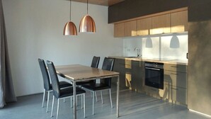 A modern kitchen with a wooden dining table and chairs, a built-in oven, and pendant lighting. - Design Ferienwohnung Nienrausch Apartment 1 (Timmendorfer Strand)