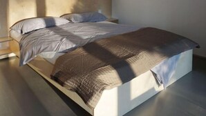 A modern bedroom with a large bed, a wooden ceiling, and a window providing natural light. - Design Ferienwohnung Nienrausch Apartment 1 (Timmendorfer Strand)