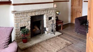A cozy living room with a stone fireplace, wooden beams, a chandelier, and a bookshelf. - Pilgrims Rest - Cheddar Guest House with Annexe (Cheddar)