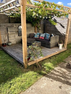 A wooden pergola with a seating area, a small table, and potted plants.