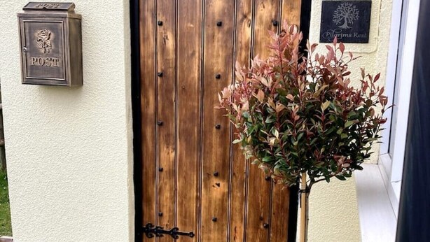 A wooden door with a black handle and a small emblem, a mailbox labeled "POST", and a plaque with a tree design. - Pilgrims Rest - Cheddar Guest House with Annexe (Cheddar)