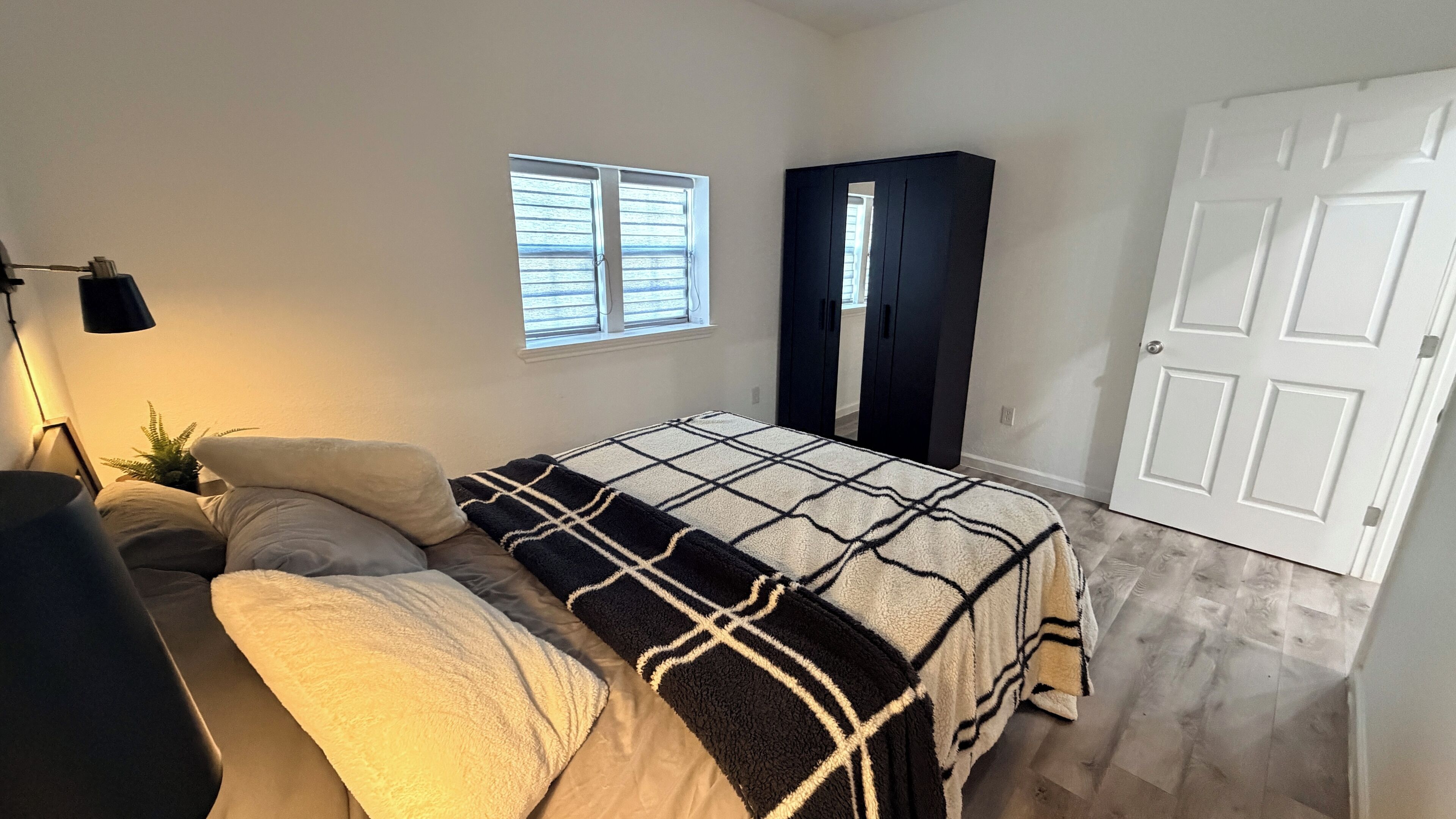 A bedroom with a bed, a nightstand, a lamp, a window, and a wardrobe.