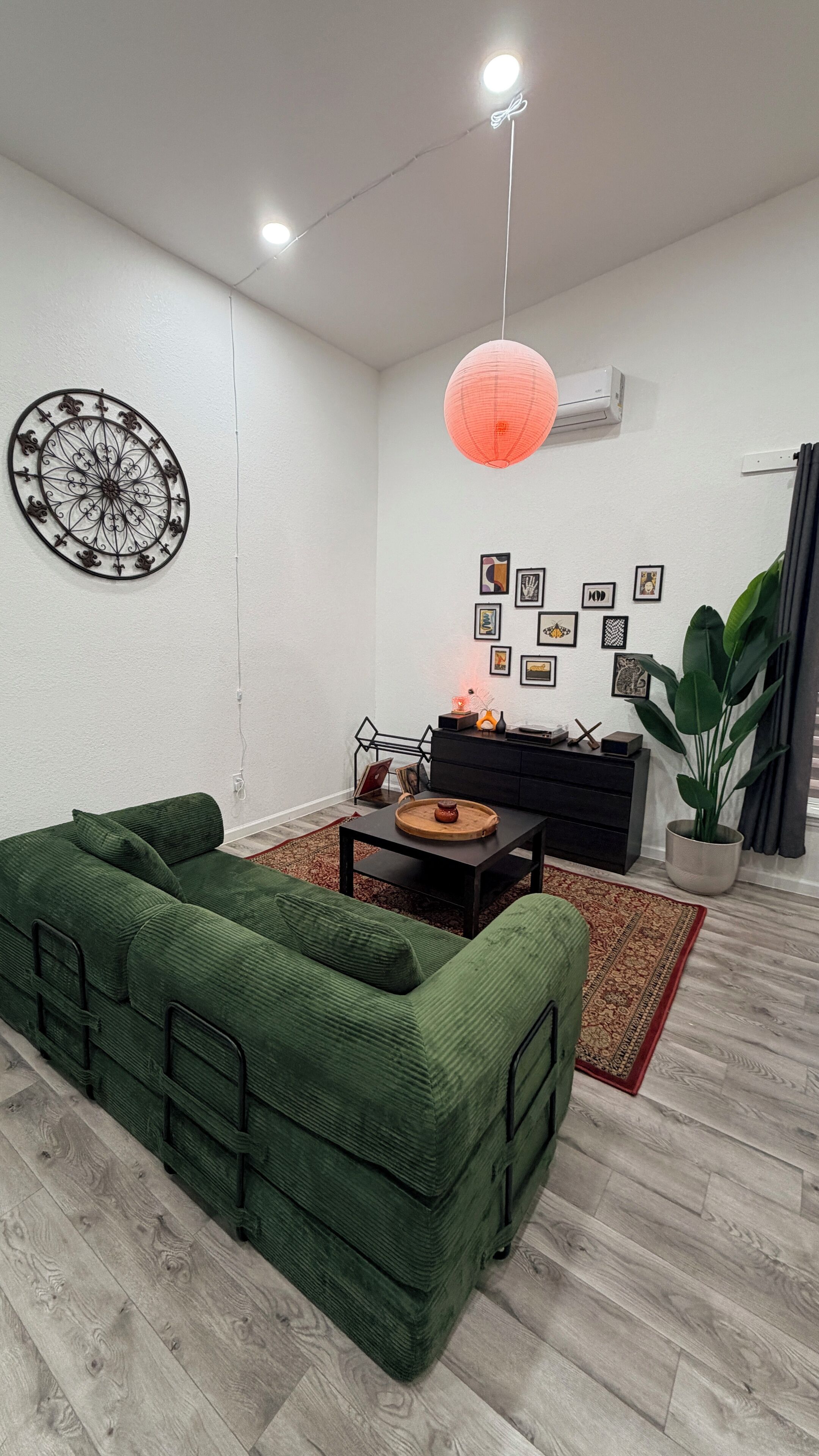 A living room with a green sofa, a coffee table, a red lantern, and a wall decorated with framed pictures.