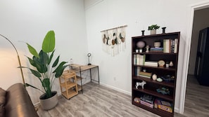 A room with a wooden floor, a bookshelf, a desk with a lamp, and a large potted plant.