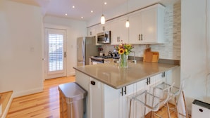 A modern kitchen with white cabinets, stainless steel appliances, and a central island with bar stools. - 2 Mi to National Mall: Stunning Townhome w/ Patio! (Washington)