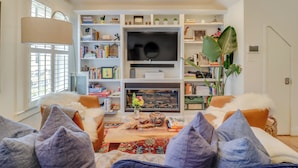 A living room with a fireplace, bookshelves, a television, and a large plant. - 2 Mi to National Mall: Stunning Townhome w/ Patio! (Washington)