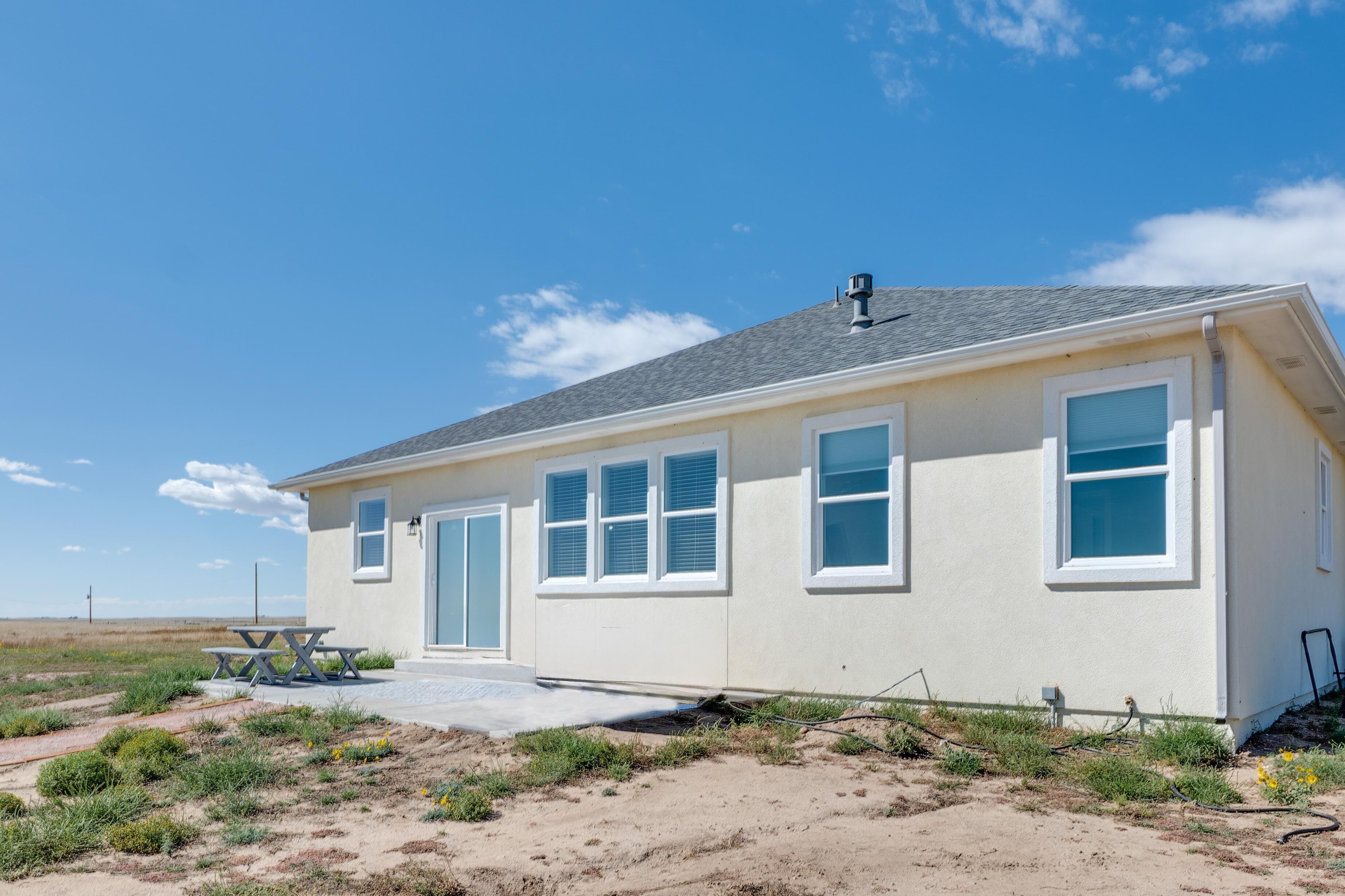A single-story house with a flat roof, large windows, and a picnic table in the front yard.